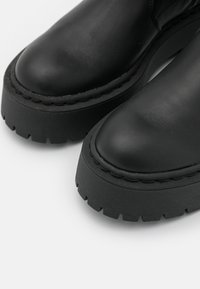 Sorte læderankle støvler med en rund tå, tyk gummisål og synlige syninger langs kanten. Tekstureret, holdbar overflade.
