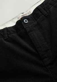 Black corduroy pants featuring a button closure, textured vertical stripes, and a plain white waistband with brand label visible.