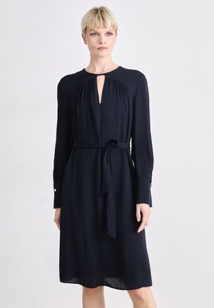 Navy blue long-sleeve dress with a keyhole neckline, tied waist, and single-button accents on sleeves; smooth, flowing fabric.