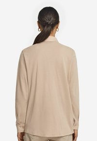Ljust beige långärmad skjorta med krage, rak skärning och knappade ärmslut. Slät textur, minimalistisk design.