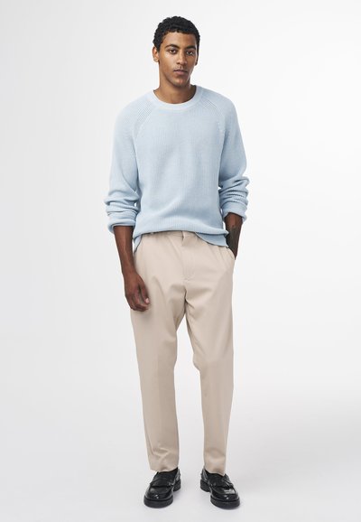 Maglione azzurro chiaro con texture, pantaloni beige e scarpe nere. Il maglione presenta un design a coste e una vestibilità rilassata; i pantaloni sono di stile a gamba dritta.