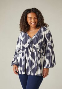 Blusa a righe navy e bianca con scollo a V, pieghe sotto il busto e maniche lunghe e morbide. Tessuto liscio con leggero lucido.