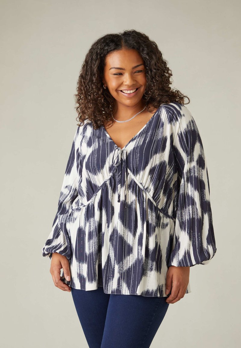 Blusa a righe navy e bianca con scollo a V, pieghe sotto il busto e maniche lunghe e morbide. Tessuto liscio con leggero lucido.