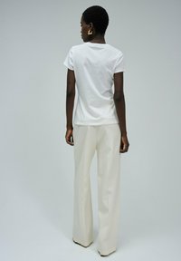 Camiseta blanca de algodón con mangas cortas, combinada con pantalones cremosos de pierna ancha y alta cintura, que presentan un diseño limpio y una textura suave.