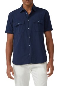 Hemd aus leichtem Stoff in Marineblau mit kurzen Ärmeln und Knopfleiste, ausgestattet mit zwei vorderen Taschen und hellblauen Knöpfen. Modell trägt weiße Hose.