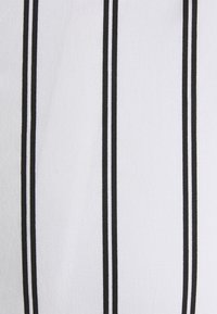 Tessuto bianco con due strisce nere verticali, caratterizzato da una superficie liscia e una trama robusta, adatto a diverse applicazioni tessili.