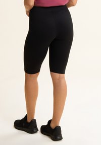 Pantalones cortos de ciclismo negros de stretch con un diseño ajustado, que llegan hasta mitad del muslo, combinados con zapatillas deportivas negras. Tejido suave con una cinturilla elástica.