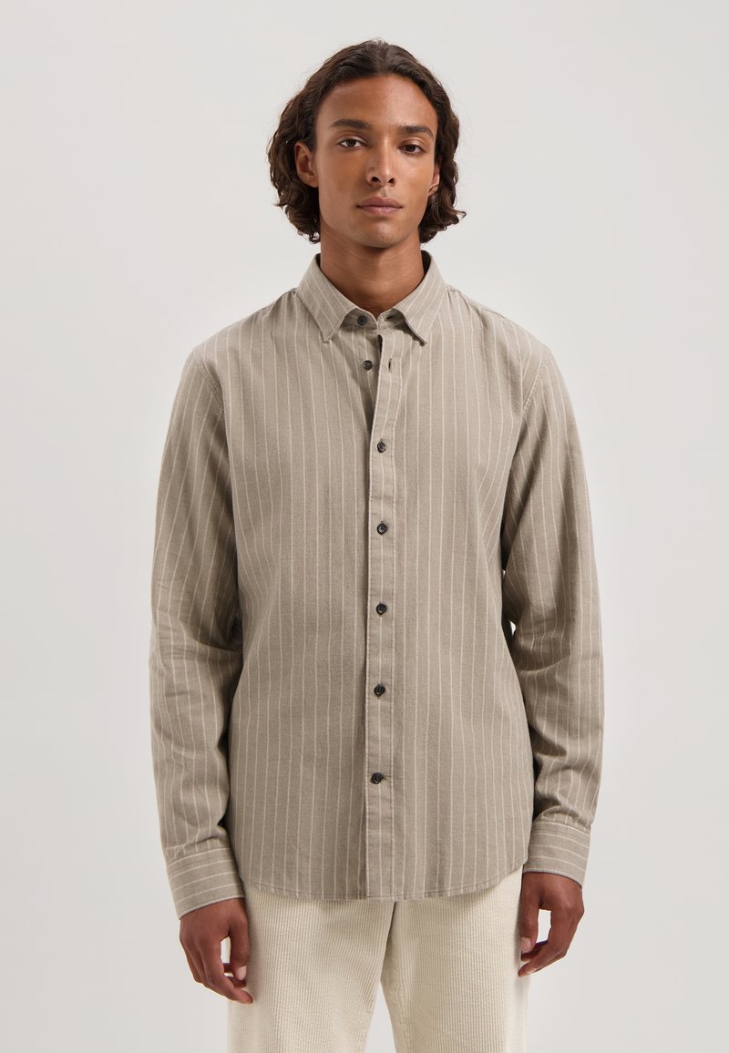 Camicia a maniche lunghe color beige chiaro con strisce bianche verticali, colletto button-down e bottoni scuri. Il tessuto sembra morbido con una finitura strutturata.