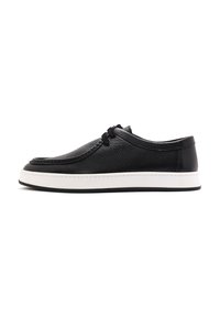 Scarpa in pelle nera con finitura texturizzata, dotata di un sottopiede bianco e suola in gomma nera, lacci elastici e design a profilo basso.