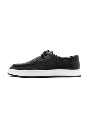 Black leather shoe with a textured finish, featuring a white midsole and black rubber outsole, elastic laces, and a low-profile design.