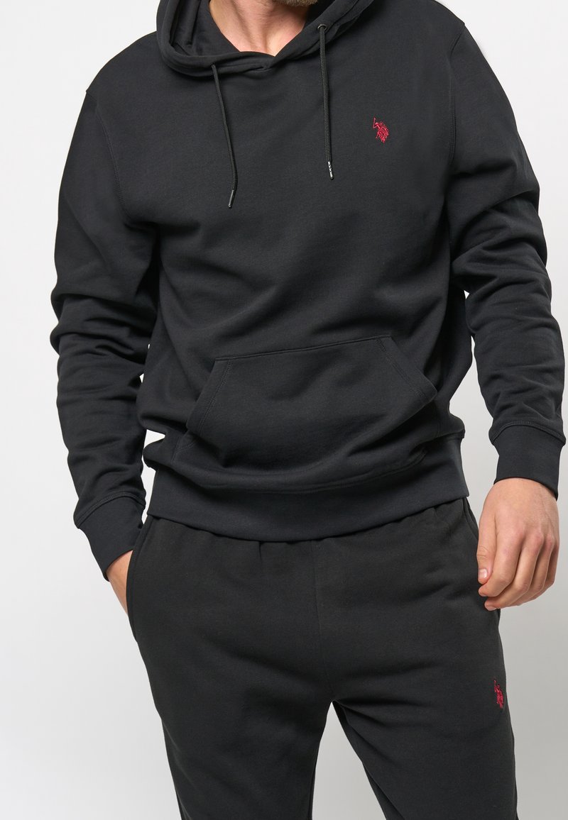Black hoodie and sweatpants set made of soft fabric; features a kangaroo pocket and red logo accent on the chest and pants.