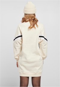 Rentouttava istuvuus, kermanvärinen college-pyddäntynä, jossa mustavalkoiset raidat hihoissa. Varustettu ribbineuloksella ja pehmeällä tekstuurilla.