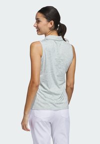 Sleeveless polo shirt in light green with a subtle pattern, featuring a collar and soft fabric, paired with white pants.