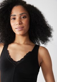 Top negro sin mangas con escote en V adornado con encaje. Tejido suave, diseño ajustado, con una textura lisa y un sutil brillo.