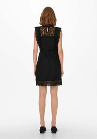 Svart spetsklänning med volangärmar, scallopad fåll och detalj med nyckelhål på ryggen. Texturerat blommönster genom hela klänningen.