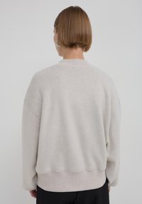 Pull oversized gris clair en tissu doux, avec un col et un ourlet côtelés, des coutures d'épaule tombantes et une coupe décontractée.