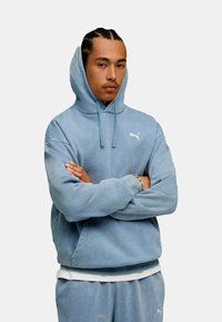 Jasnoniebieska hoodie wykonana z miękkiego materiału, z kangurzą kieszenią i białym logo na piersi. Wygodne, luźne dopasowanie.