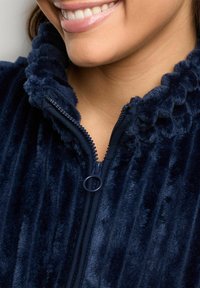 Giacca in pile blu navy con zip e texture a costine, colletto morbido. Presenta una zip a contrasto e un tessuto soffice adatto per il calore.