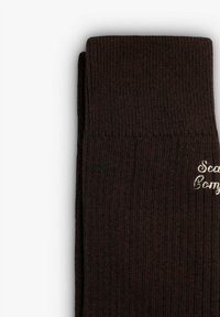 Calze di lana marroni con una trama a coste, dotate di un risvolto e di un ricamo con la scritta "Scandi Comfy". Materiale morbido ed elastico.
