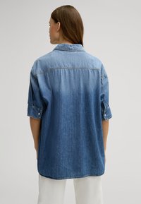 Denim shirt in medium blue, featuring a collar, rolled sleeves, and a relaxed fit with a straight hem. Soft texture and classic styling.