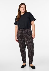 T-shirt noir à manches courtes associé à un pantalon imprimé léopard marron. Le pantalon a une taille élastique et des poignets fuselés. Ballerines noires.
