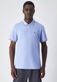 Jasnoniebieska koszulka polo z gładkiego materiału, z plastronem na dwa guziki, czarno-białymi wykończeniami kołnierzyka i rękawów oraz logiem.