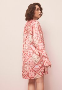 Hosszú ujjú, térdig érő rózsaszín ruha mintás kialakítással, amely szíveket és virágmotívumokat ábrázol különböző piros árnyalatokban, puha anyagból készült.