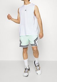 Hvid ærmeløs skjorte med sort logo, kombineret med mintgrønne shorts med sorte og hvide striber og et mesh-look. Atletiske sko.