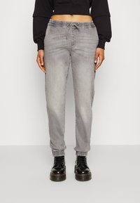 Pantalones de chándal grises con cintura elástica y cordón, que presentan un corte relajado y tobillos acampanados, combinados con botas negras de cordones.