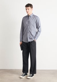 Light blue chambray button-up shirt with long sleeves, paired with black tailored pants and black sneakers. Holding a black clutch.