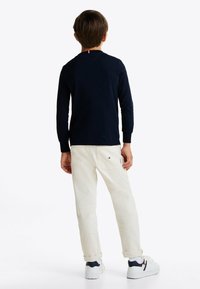Langärmliges Navy-T-Shirt mit Rundhalsausschnitt, kombiniert mit cremefarbener Hose. Abgerundet mit weißen Sneakern mit navy- und roten Akzenten.