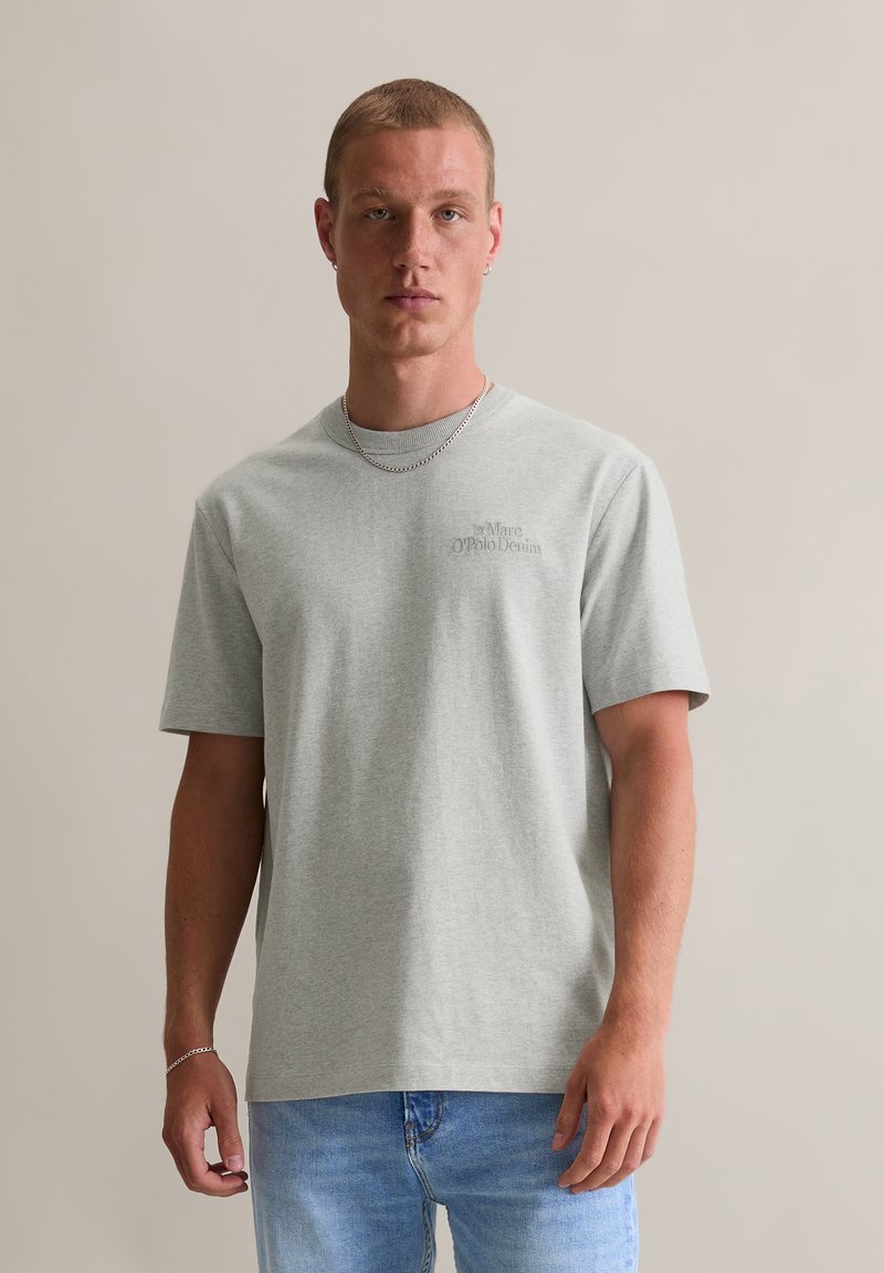 T-shirt en coton gris clair à manches courtes, col rond, avec impression de logo sur le devant. Associé à un jean en denim bleu clair. Style simple et décontracté.