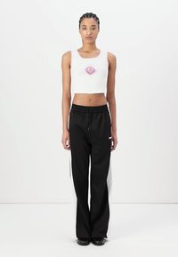 Hvit, avskåret tanktop med et grafikk av et lilla hjerte, kombinert med svart og hvite joggebukser med elastisk liv og snøring.