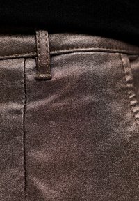 Metallisch bronze Hosen mit glatter Textur, ausgestattet mit einem Gürtelschlaufe und sichtbarem Nähten entlang der Nähte. Nahaufnahme des Stoffs.