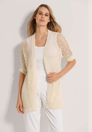 Cardigan en tricot ouvert de couleur beige clair avec des manches courtes, présentant un design en crochet lâche et une bordure côtelée le long des bords.
