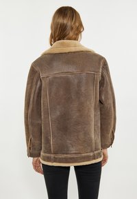 Giubbotto in shearling marrone con colletto beige morbido, dalla forma squadrata e con fibbie laterali, realizzato in pelle texturizzata con fodera in lana.