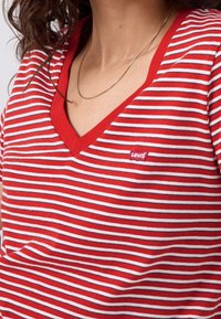 Femme portant un t-shirt à rayures rouges et blanches en V avec un petit logo Levi's sur la poitrine et un fin collier en chaîne dorée.