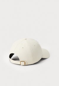 Cream-colored baseball cap with a curved brim, adjustable strap at the back, and six ventilation holes on the crown.