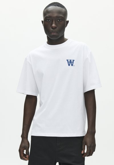 Λευκό βαμβακερό T-shirt με χαλαρή εφαρμογή, που διαθέτει μπλε λογότυπο "W" στο αριστερό στήθος. Κοντά μανίκια και στρογγυλή λαιμόκοψη.
