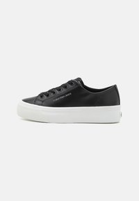 Sorte faux skinn sneakers med hvit gummisåle, rund tå, seks hull snøring, og "Calvin Klein Jeans" logo på siden.