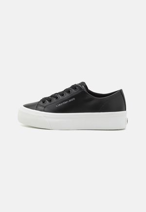 Black faux leather sneaker with white rubber sole, round toe, six eyelet lace-up closure, and "Calvin Klein Jeans" logo on the side.