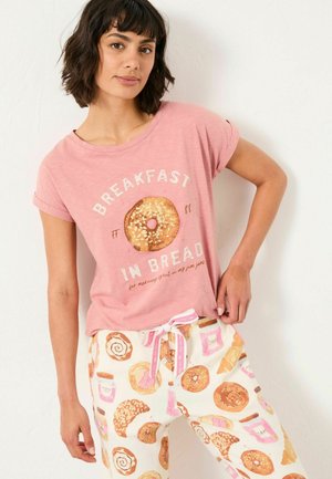 Pink short-sleeve t-shirt with donut graphic and text "Breakfast in Bread," paired with light-colored pajama pants featuring assorted pastry prints.