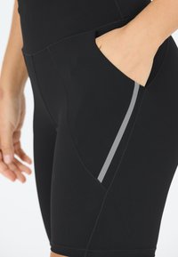 Zwarte sportshorts met een gladde textuur, voorzien van een zijzak en een grijze accentstreep langs de naad.