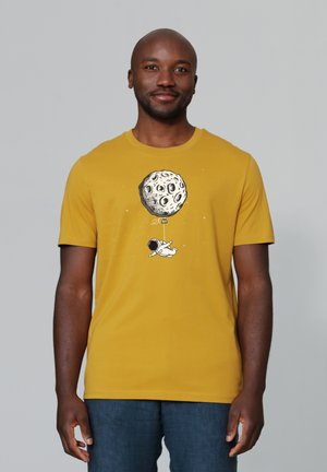 Gele katoenen t-shirt met een grafisch ontwerp van een astronaut met een ballon vast aan een gestructureerde, gedetailleerde maan. Korte mouwen, ronde hals.