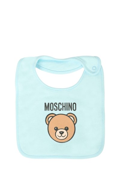 Bavaglino azzurro chiaro in morbido cotone, con una grafica della faccia di un orso in marrone e nero, accompagnata dal testo "MOSCHINO" sopra. Chiusura a pressione sul collo.