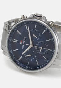 Montre en acier inoxydable avec un cadran bleu marine, des aiguilles argentées et un affichage de la date. Dispose d'un chronographe et d'une lunette texturée.
