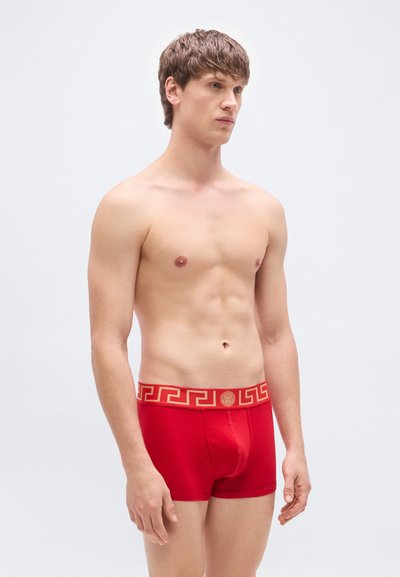 Κόκκινα βαμβακερά μποξεράκια με ζώνη μέσης διακοσμημένη με χρυσές λεπτομέρειες και μοτίβο ελληνικού κλειδιού. Λείο υλικό, εφαρμοστό σχέδιο, μινιμαλιστικό στυλ.