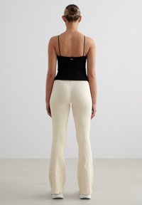 Haut noir ajusté à fines bretelles associé à un pantalon crème évasé présentant une texture à côtes verticales. Modèle vu de dos.