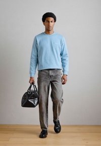 Sweater azul claro de gola redonda, jeans largos cinzentos, sapatos pretos e uma bolsa preta texturizada com alças duplas. Design simples e moderno.