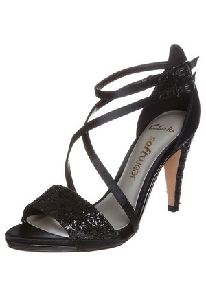 Musta korkeakorkoinen sandaali avoimella varpaan muotoilulla. Koristeena paljettiyksityiskohtia, ristiin menevät hihnat ja tyylikäs stiletto-korko. Sileä pinta.
